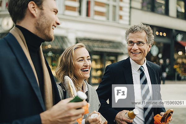 Smiling business colleagues discussing while holding food and drink in city