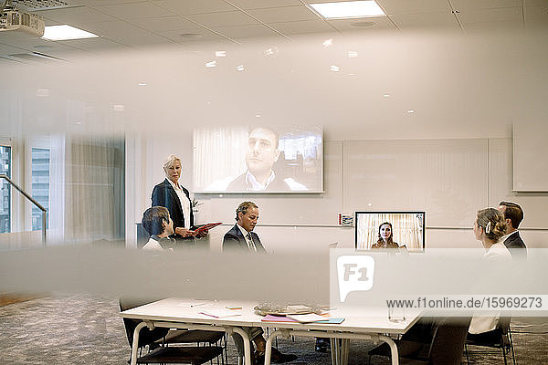 Male and female executives discussing in web conference meeting seen through glass at workplace
