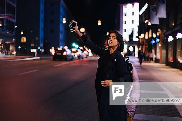 Junge Frau mit Telefon ruft nachts in der Stadt nach einem Taxi
