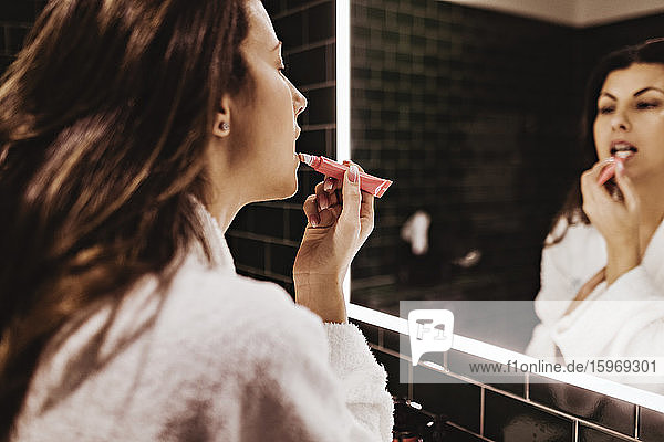 Mittelgroße erwachsene Frau  die in den Spiegel schaut  während sie im Hotel Lippenstift aufträgt