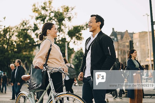 Lächelnde Frau mit Fahrrad  die einen männlichen Freund ansieht  während sie in der Stadt steht