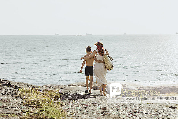 Rear view of woman with son walking against sea during sunny day