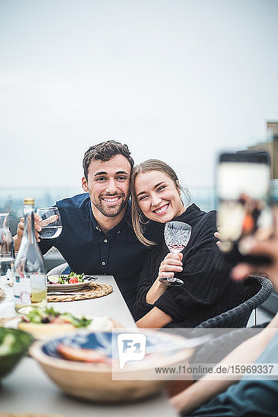 Glückliche Freunde mit Getränken die während der Dachparty zum Fotografieren posieren