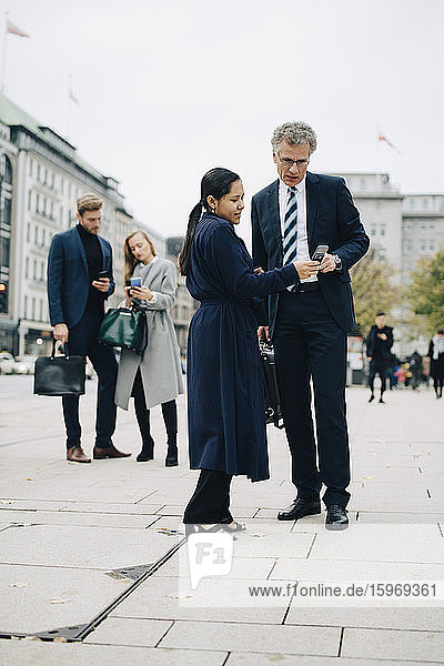 Unternehmerinnen und Unternehmer  die ein Smartphone benutzen  während sie in der Stadt auf der Straße stehen