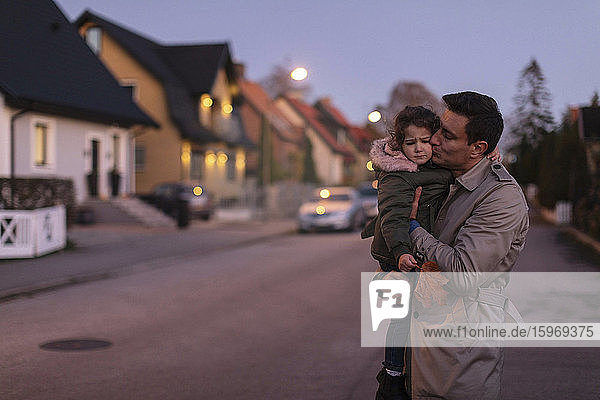 Vater umarmt und küsst traurige Tochter  während er bei Sonnenuntergang im Freien steht