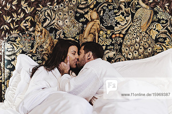 Paar küsst sich im Hotelzimmer auf dem Bett liegend