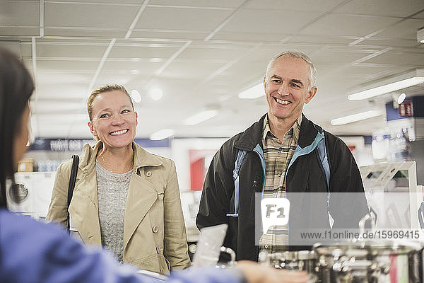 Smiling mature customers looking at young owner in store