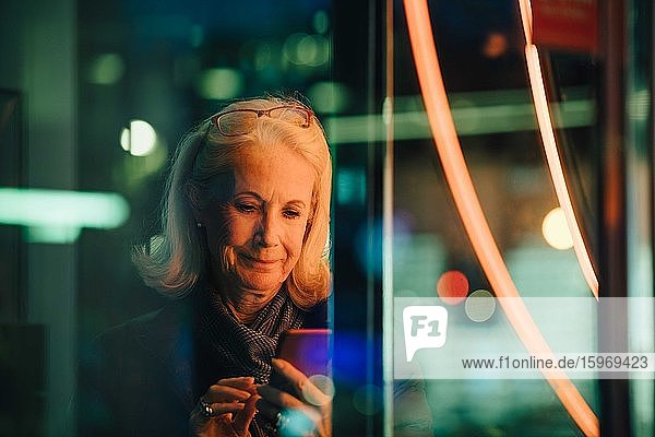 Wrinkled woman using smart phone while standing in city at night