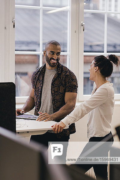 Lächelnde kreative Geschäftskollegen  die mit einem digitalen Tablet am Schreibtisch im Büro arbeiten