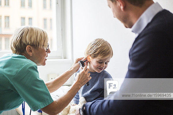 Ärztin untersucht das Ohr des Jungen mit dem Otoskop  während sie im Krankenhaus beim Vater sitzt