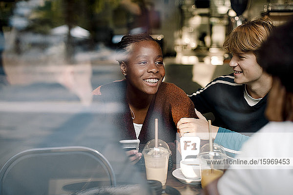 Smiling teenage girl with friends at cafe seen through glass window