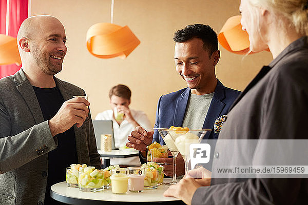 Lächelnde Geschäftsleute unterhalten sich beim Essen im Büroseminar