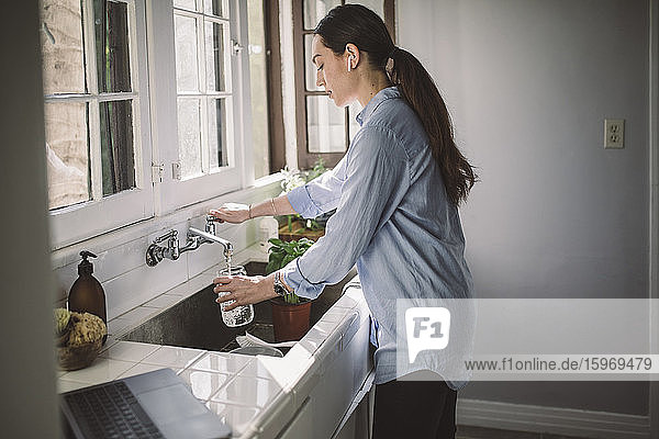 Seitenansicht einer weiblichen Geschäftsfrau  die Wasser in einen Krug an der Küchenspüle füllt