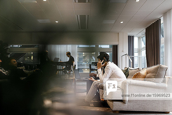 Geschäftsmann spricht am Mobiltelefon  während er mit Kollegen bei einer Besprechung während einer globalen Konferenz im Büro sitzt