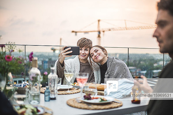 Smiling female friends taking selfie with blanket while sitting at rooftop during social gathering