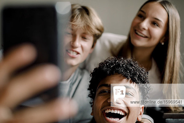 Fröhliche männliche und weibliche Freunde im Teenageralter  die sich mit dem Handy zu Hause selbstständig machen