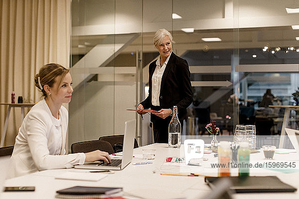 Reife Fachkraft bespricht Strategie  während eine Kollegin bei einem globalen Geschäftstreffen am Laptop sitzt