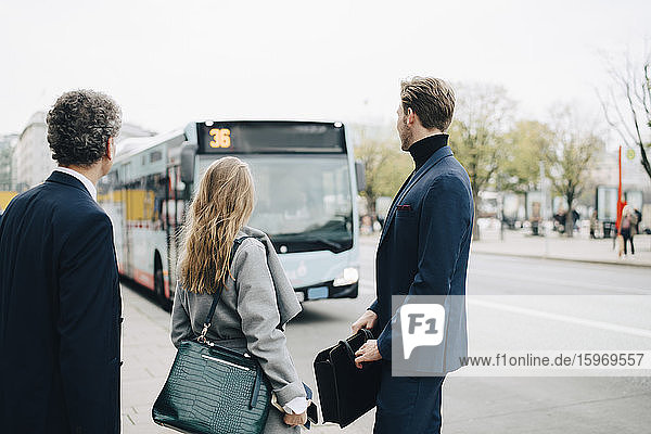 Unternehmerinnen mit männlichen Mitarbeitern  die in der Stadt stehend auf den Bus schauen