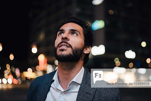 Contemplating man looking up while standing in city at night