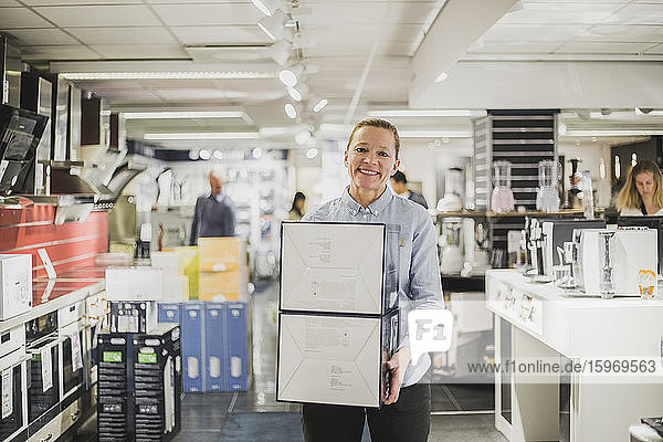 Porträt einer lächelnden  reifen Besitzerin mit Kisten im Elektronikladen