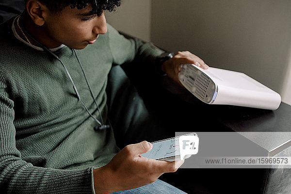 Teenager hält Router in der Hand  während er zu Hause die Wi-Fi-Verbindung auf seinem Mobiltelefon überprüft