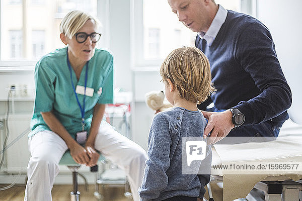 Rückansicht eines Jungen  der beim Vater steht  während er in der Klinik mit dem Arzt spricht