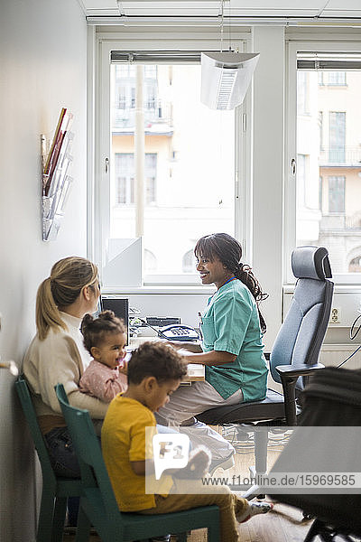 Smiling pediatrician talking to mother while children sitting in clinic