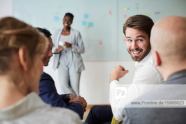 Lächelnder Geschäftsmann schaut männlichen Kollegen während einer Präsentation an  während er im Büroseminar sitzt