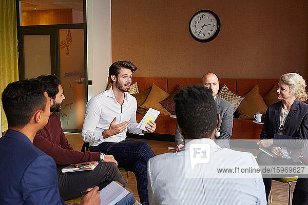 Male entrepreneurs discussing with coworkers while sitting in circle during office workshop