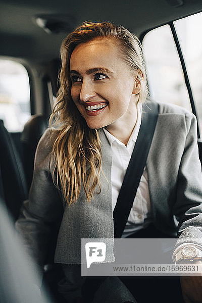 Lächelnder Unternehmer schaut weg  während er im Taxi angeschnallt ist