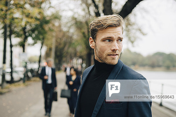 Contemplating businessman looking away while standing in city