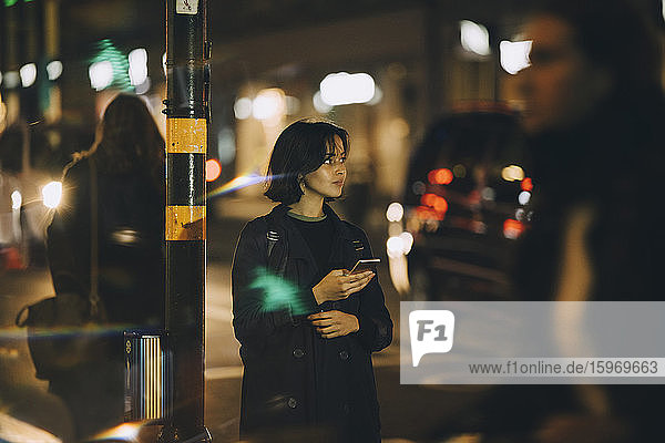 Junge Frau schaut weg  wenn sie nachts in der Stadt ein Handy benutzt