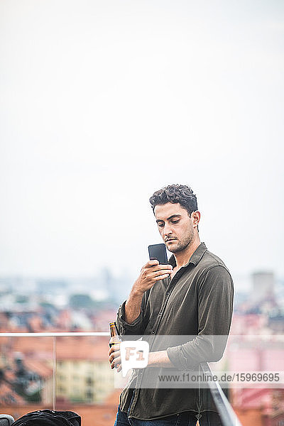 Mann benutzt Smartphone  während er auf der Terrasse gegen den Himmel steht