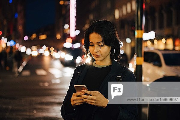 Young woman using mobile phone while standing in city at night