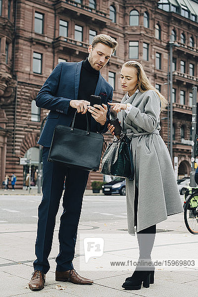 Businessman and businesswoman using phone while standing in city