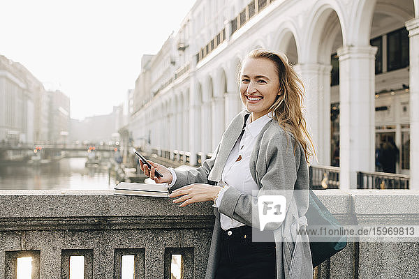 Porträt einer Geschäftsfrau mit Smartphone an einer Stützmauer in der Stadt