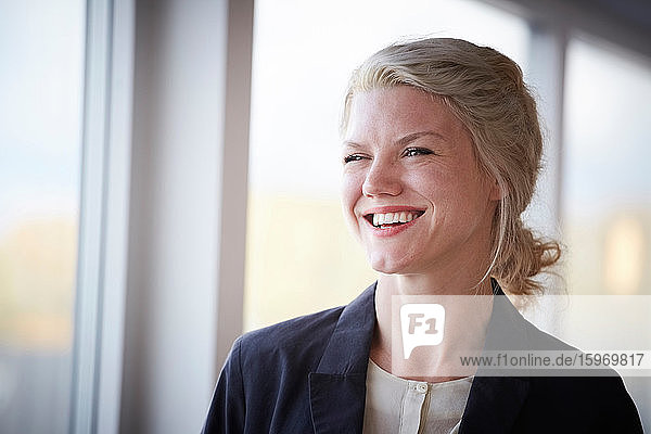 Lächelnde selbstbewusste Geschäftsfrau  die am Arbeitsplatz wegschaut