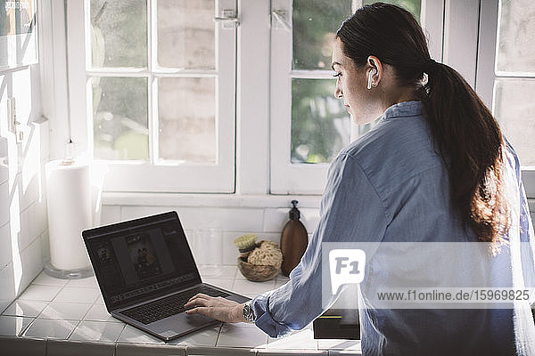 Rückansicht einer weiblichen Fachkraft  die einen Laptop am Schalter im Heimbüro benutzt