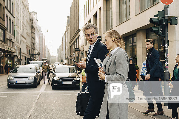 Seitenansicht eines weiblichen Geschäftsmannes mit einem männlichen Mitarbeiter beim Überqueren der Straße in der Stadt