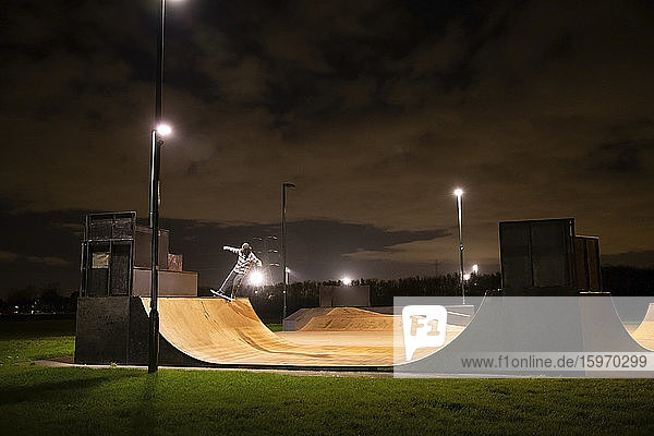 Junger Mann fährt nachts Skateboard auf Skatepark-Rampe