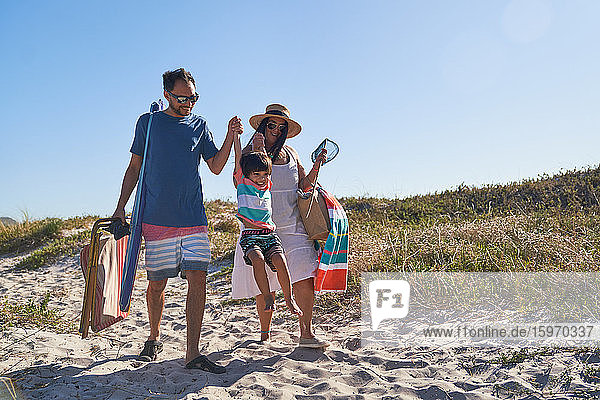 Verspielte Familie beim Spaziergang im Sand auf einem sonnigen Strandweg
