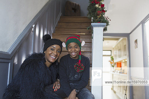 Porträt einer glücklichen Mutter und ihres Sohnes mit Weihnachtshüten auf der Treppe