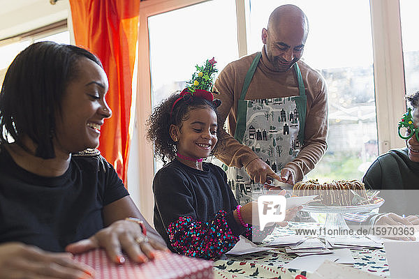 Glückliche Familie packt Weihnachtsgeschenke ein und schreibt Karten bei Tisch