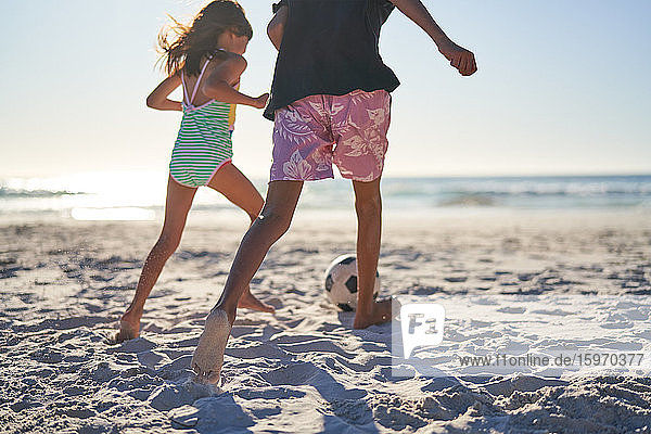 Brother and sister playing soccer on sunny beach