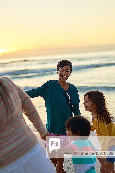 Glückliche Familie spielt am Strand bei Sonnenuntergang