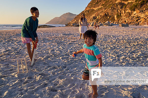 Porträt einer glücklichen Familie beim Kricketspielen am sonnigen Strand