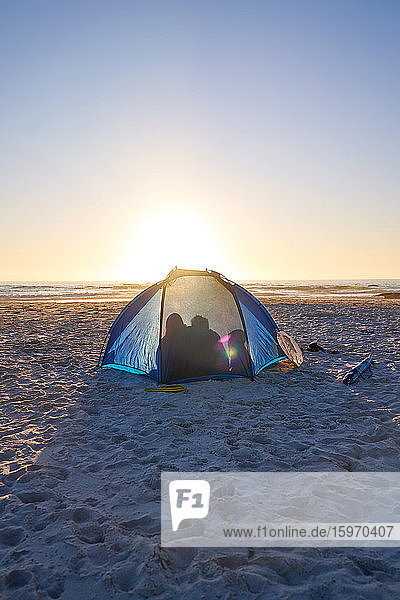 Silhouette family inside tent on sunny sunset beach