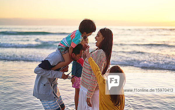 Glückliche Familie watet am Strand bei Sonnenuntergang in der Brandung