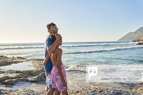 Portrait glücklicher Vater und Sohn beim Spaziergang am sonnigen Strand des Ozeans