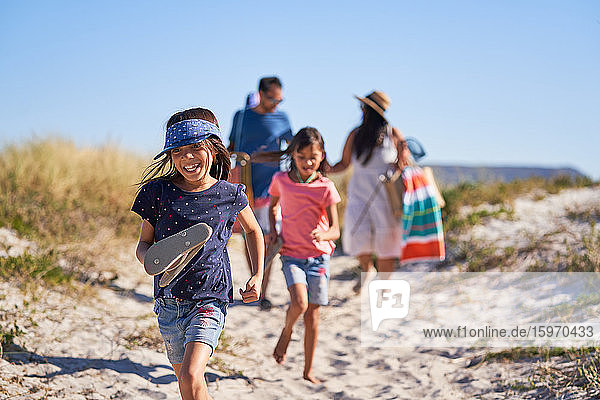 Glückliches Mädchen läuft mit Familie am sonnigen Strand